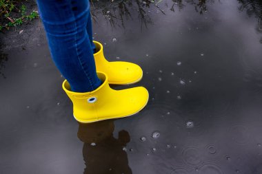 Su birikintisinde duran sarı lastik çizmeli kadın.
