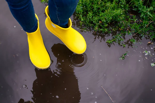 Woman in yellow rubber boots going through the puddle.