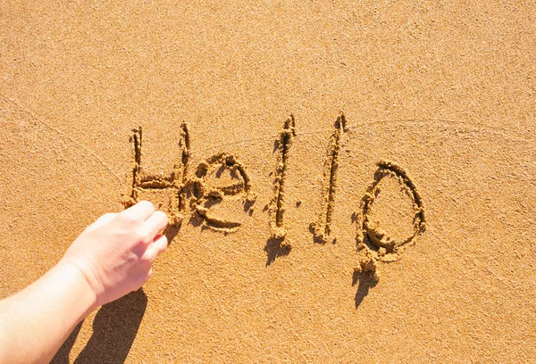 Woman hand written Word Hello on sea sand.