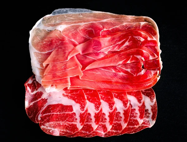 Plakken salami en prosciutto op zwarte achtergrond. — Stockfoto