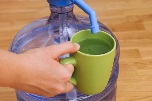 Vrouw hand met kopje vol water in de buurt van fles met waterpomp. — Stockfoto