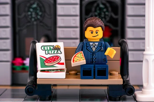 Lego-Geschäftsmann isst Pizza auf der Bank draußen. — Stockfoto