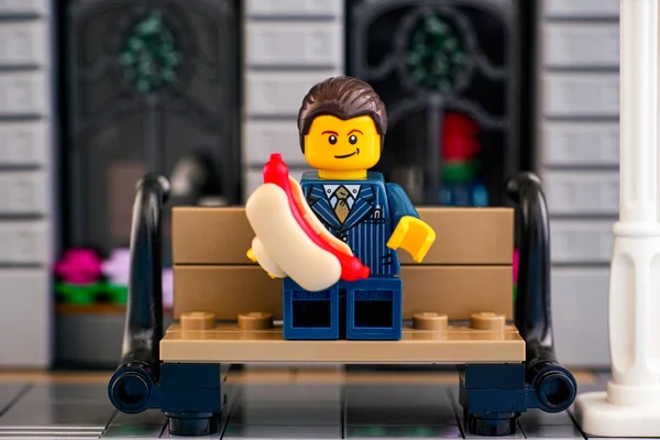 Лего бизнесмен ест хот-доги на скамейке снаружи . — стоковое фото