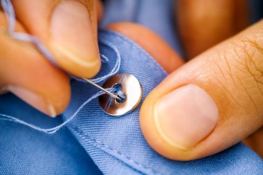 Bir düğme diken kadın parmaklarının yakın çekimi.