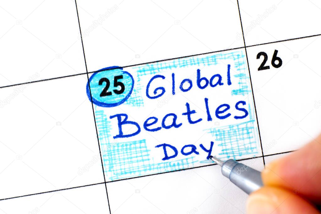 Woman fingers with pen writing reminder Global Beatles Day in calendar. June 25.