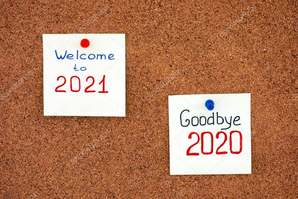 Two notes with phrases Goodbye 2020 and Welcome to 2021 on corkboard.