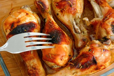 Kızarmış tavuk budu, cam fırın tepsisinde, çatalla birlikte yenmeye hazır. Yakın plan.