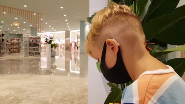 Kleiner Junge mit Maske sitzt in Einkaufszentrum