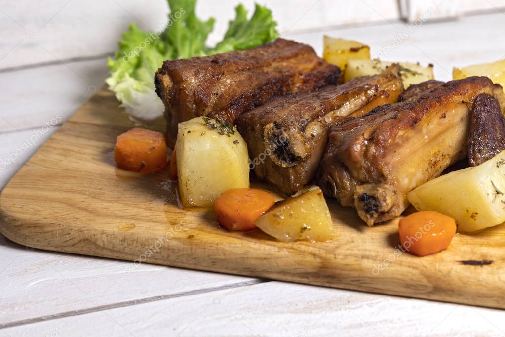 Roasted pork ribs with thyme potatoes over white wooden background, Eastern cuisine