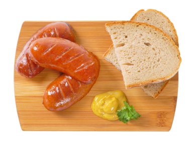 short thick sausages with slices of bread and mustard on wooden cutting board clipart
