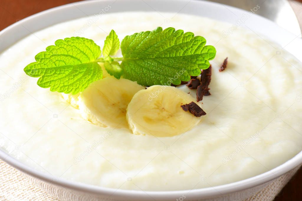 Bowl of smooth milk pudding with sliced banana and grated chocolate