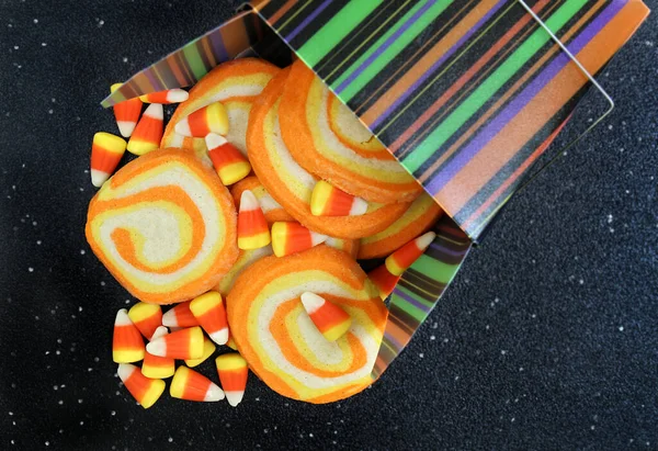 Candy corn swirled cookies and candy corn coming out of a colorful fall striped Chinese container.  Top view, macro image.