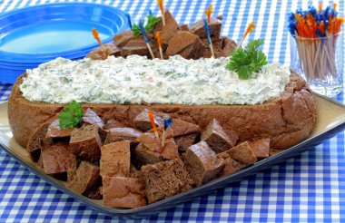 Spinach dip in an oval loaf of pumpernickel bread, with bread cubes for dipping. clipart