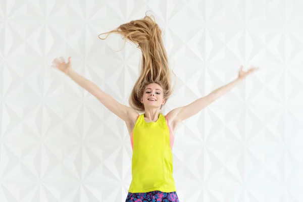 Nahaufnahme einer fröhlich springenden, fitten Frau mit langen Haaren vor weißer Wand — Stockfoto