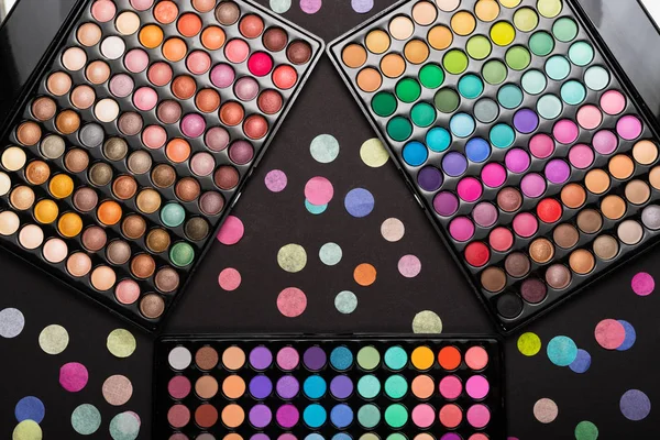 Palettes de maquillage colorées et confettis colorés sur fond noir — Photo