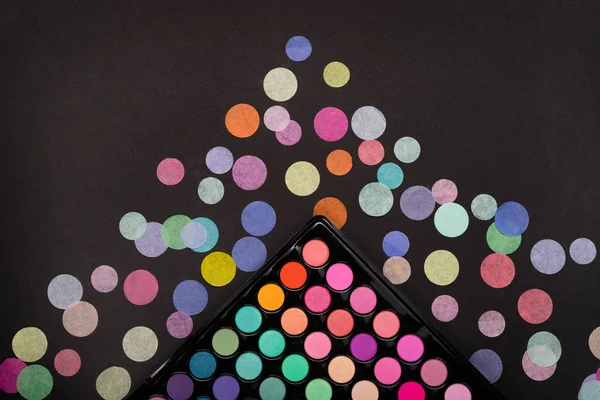 Vista dall'alto della tavolozza di ombretti make-up con confetti sparsi sul nero — Foto Stock