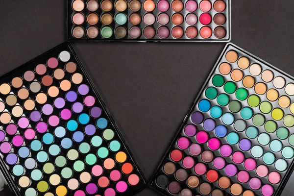 Make-up frame made of colorful eyeshadow palettes arranged as triangle on black — Stock Photo, Image