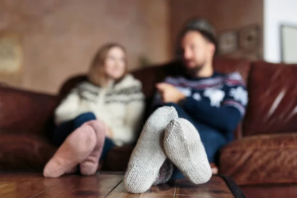 Mladý muž a žena na sobě ponožky vánoční rozhovor a zároveň sedí na gauči doma — Stock fotografie