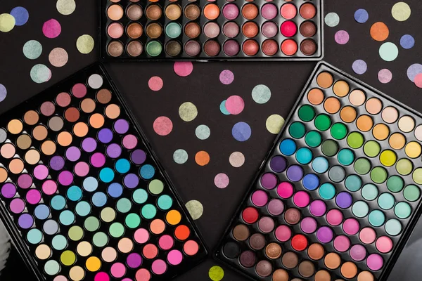 Make-up eyeshadow palettes with confetti scattered on black — Stock Photo, Image