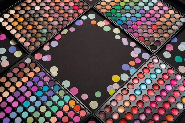 Make-up eyeshadow palettes with confetti scattered on black — Stock Photo, Image