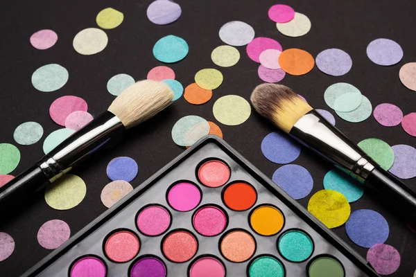 Primer plano de los pinceles de maquillaje con colorida paleta de maquillaje y confeti dispersos — Foto de Stock