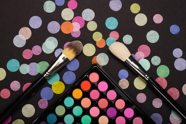 Make-up palette with make-up brushes with colorful confetti on black background — Stock Photo, Image