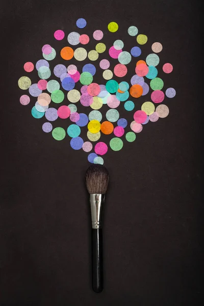 Pincel de maquiagem com confete colorido espalhado no fundo preto — Fotografia de Stock