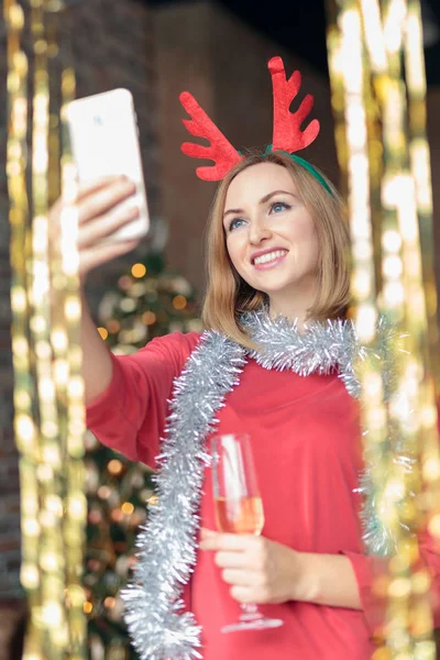 Young happy woman drinking champagne and taking selfie at New Years party