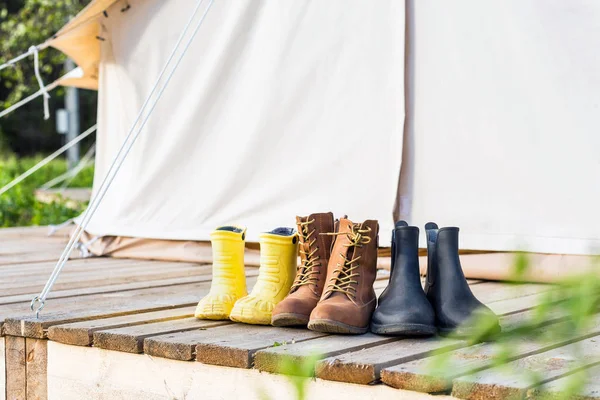 Three pair of shoes on wooden terrace behind a canvas tent — Stock Photo, Image