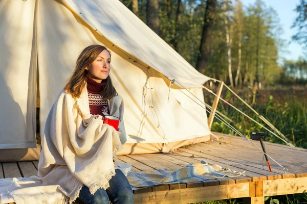 Ung kvinna sveper filten över sig själv när man dricker kaffe nära duk bell tält — Stockfoto
