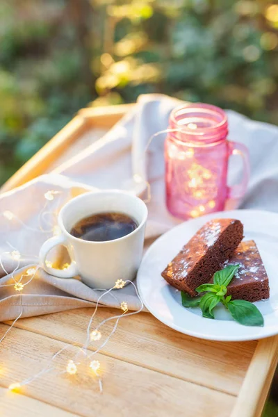 Tazza di tè con una torta di brownie decorata con menta su un vassoio di legno all'aperto decorato con una bella luce — Foto Stock