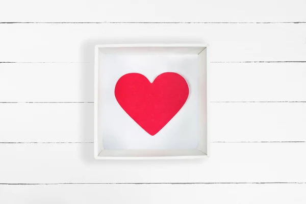 Червоне паперове серце в білій картонній коробці на білому дерев'яному фоні — стокове фото