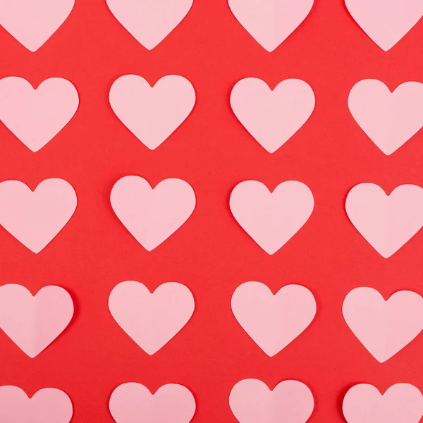 Pink paper hearts arranged in rows on red background. Flat lay — Stock Photo, Image