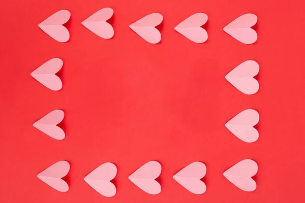 Flat lay of pink paper hearts arranged as a frame on red background — Stock Photo, Image