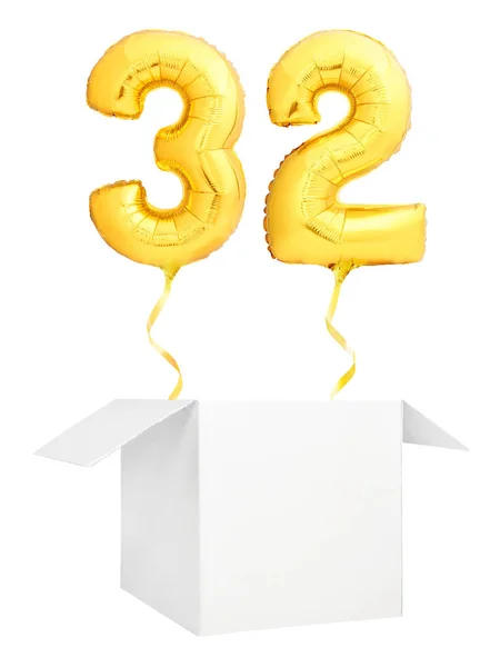Золотой номер тридцать два надувных шарика с золотой лентой, летящей из пустой белой коробки, изолированной на белом фоне — стоковое фото