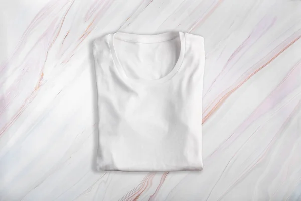 Branco em branco t-shirt dobrada no fundo de mármore — Fotografia de Stock