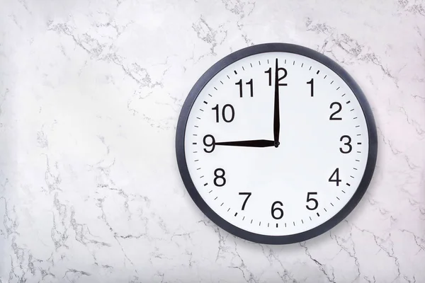 Настенные часы показывают девять часов на текстуре белого мрамора. Часы в офисе показывают 9 вечера или 9 утра — стоковое фото