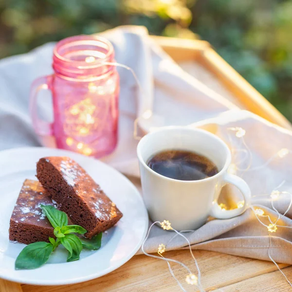 Крупный план чашки чая с пирожным, украшенным мятой на деревянном столе на открытом воздухе — стоковое фото