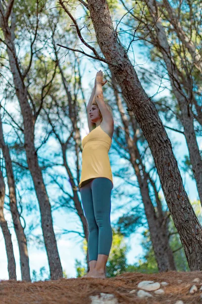 Szczęśliwa młoda kobieta ćwicząca jogę z podniesionymi rękami w lesie na zewnątrz. Postawa salutowa w górę — Zdjęcie stockowe
