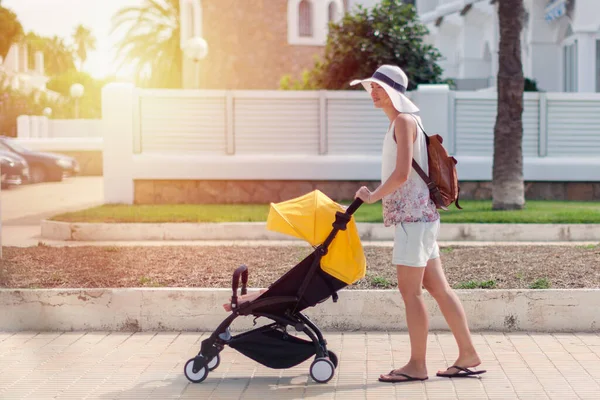Young mother pushing stroller with sleeping baby outdoors — Stock Photo, Image