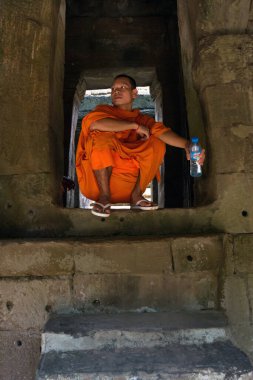 Turuncu cüppeli keşiş Angkor Wat tapınağında elinde plastik bir şişe su tutarken oturuyor.