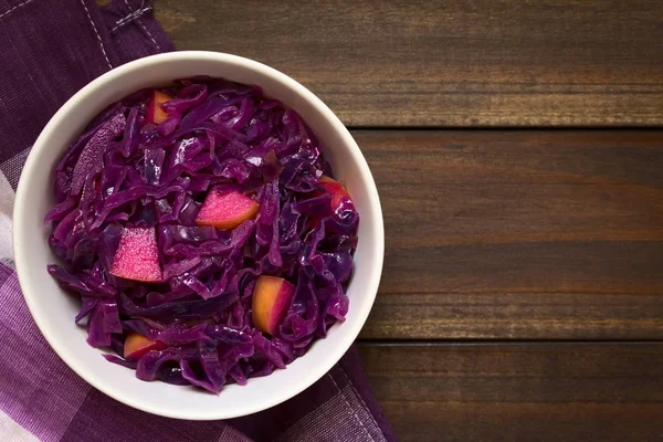 Braised red cabbage with apple in bowl, photographed overhead on dark wood with natural light (Selective Focus, Focus on the top of the dish)