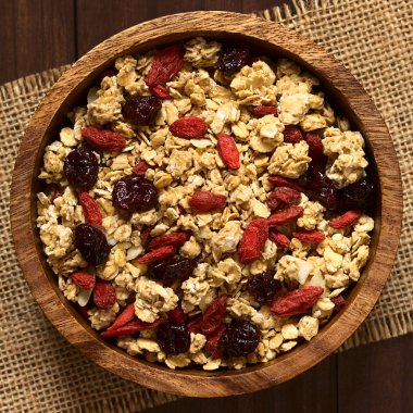 Badem ve kurutulmuş goji meyveleri ve ahşap kase, cranberries ile gevrek yulaf ezmesi tahıl fotoğrafı doğal ışık (seçici odak, odak üstünde tahıl ile ek yükü)