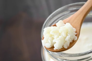 Süt kefir taneleri üzerinde tahta kaşık kefir doğal ışık (seçici odak, odak ortasında kefir taneleri ile fotoğraflandı, bir kavanoz üstünde)