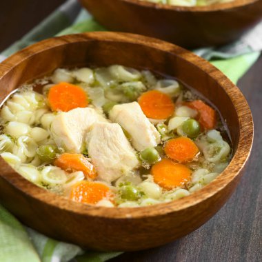 Ev yapımı tavuk çorbası bezelye, havuç ve ahşap kase, küçük kabuk makarna ile fotoğraflandı doğal ışık (seçici odak, odak tavuk çorbası ön ile)