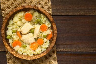 Bezelye, havuç ve ek yükü üzerinde koyu renkli ahşap doğal ışık (seçici odak, odak üstünde çorba ile fotoğraflandı küçük kabuk makarna ahşap kase, ev yapımı tavuk çorbası)