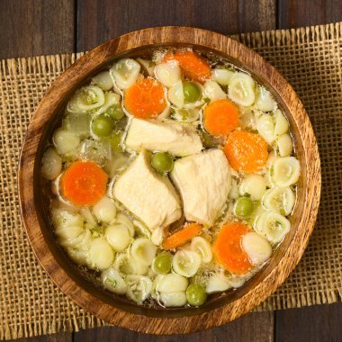 Bezelye, havuç ve ek yükü üzerinde koyu renkli ahşap doğal ışık (seçici odak, odak üstünde çorba ile fotoğraflandı küçük kabuk makarna ahşap kase, ev yapımı tavuk çorbası)