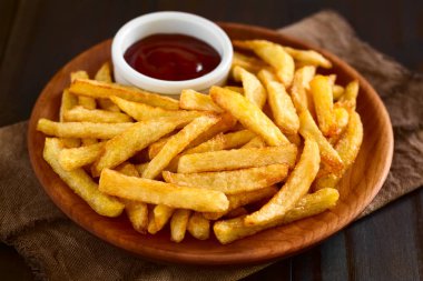 Taze ev yapımı gevrek patates kızartması ketçap ahşap plaka üzerinde küçük bir kase ile fotoğraflandı doğal ışık (seçici odak, odak üçte içine patates kızartması ile)