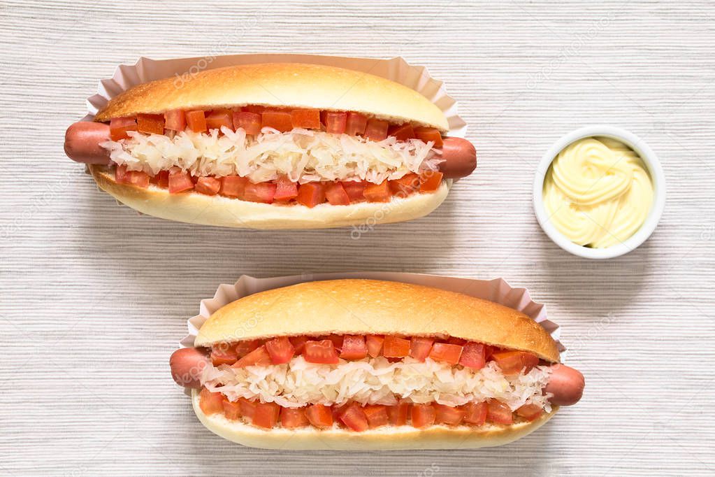Chilean Completo Clasico (classical) or Completo Aleman (German) traditional hot dog sandwiches, made of bread, sausage, tomato cubes and sauerkraut, mayonnaise in small bowl on the side, photographed overhead with natural light  