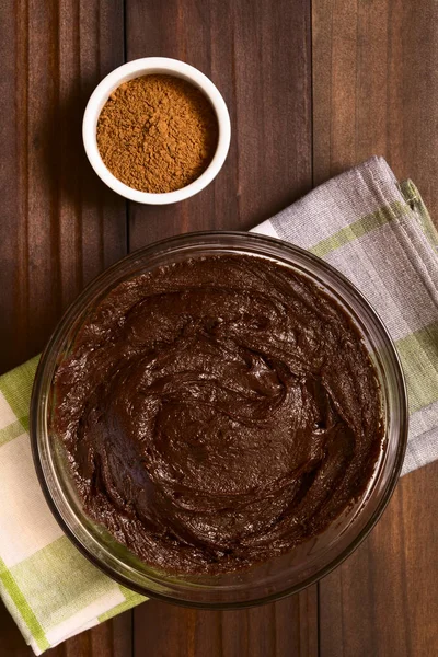 Basic brownie, chocolate cake or cookie dough in glass bowl with cocoa powder on the side, photographed overhead on dark wood with natural light (Selective Focus, Focus on the top of the dough)
